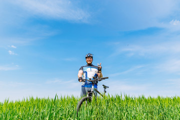 young adult smiling man standing with bicycle in green barley fi