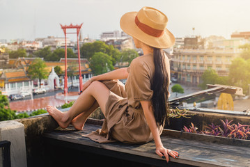 Woman tourists in hat and brown dress enjoyed the view of Giant swing and Sutat Temple landmark of Bangkok city in sunset time ,Sao Ching Cha and Temple of Buddha at dusklandmark of Thailand