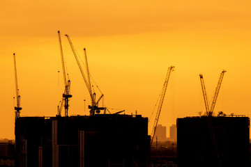 Silhouette large construction site including several cranes working on a building, tower cranes against on sunset time background at Bangkok city Thailand