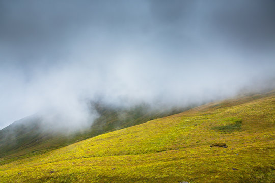 Lush green landscape under a foggy cloud cover in the Annapurna valley near base camp, Nepal.