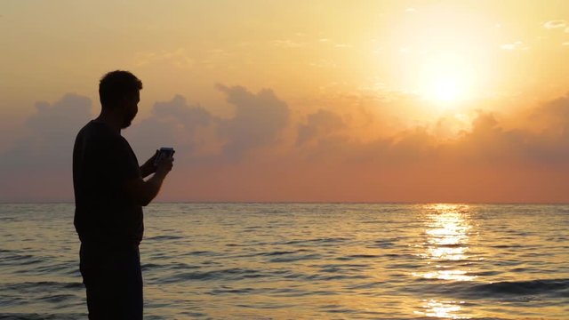 Black silhouette of adult tall man taking pictures of beautiful scenic seascape and selfie during sunrise on early morning. Real time full hd video footage.