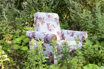 Old armchair in an abandoned garden amid tall grass