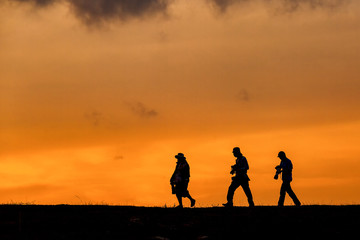 silhouette of photographer group walking with camera for taking photo during sunset