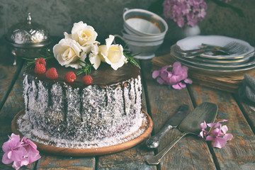 Gluten-free and dairy-free cake decorated with white roses and coconut: chocolate-nut biscuit, berry mousse, custard on almond milk and chocolate glaze. Healthy dietary baking. Vegetarian food.