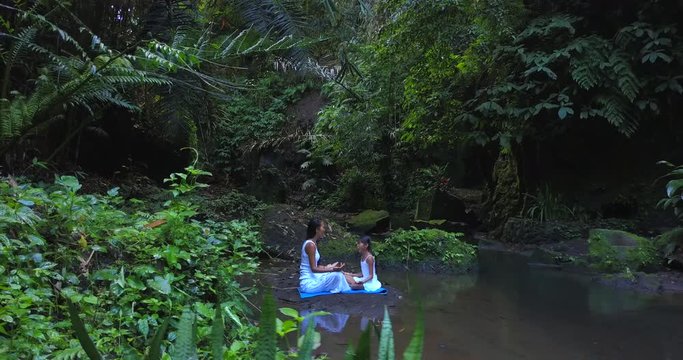 Mother with daughter learn the practice of meditation,sit near sacred nature place,waterfall, pond and deep jungle around,concept of thoughts and concentration 