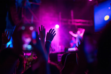 Crowd of audience with hands raised at a music festival. Lights streaming down from above the stage