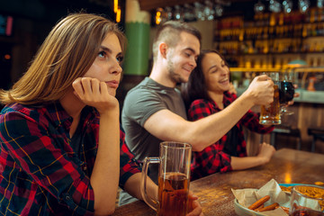 people, leisure, friendship and communication concept - happy friends drinking beer, talking and clinking glasses at bar or pub