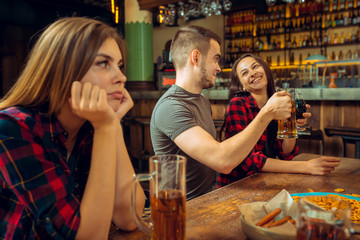 people, leisure, friendship and communication concept - happy friends drinking beer, talking and clinking glasses at bar or pub