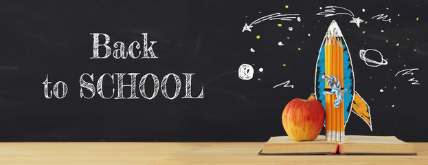 Back to school banner. rocket sketch and pencils over open book in front of classroom blackboard.
