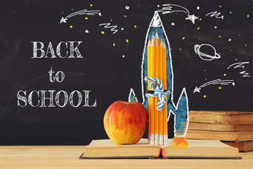 Back to school concept. rocket sketch and pencils over open book in front of classroom blackboard.