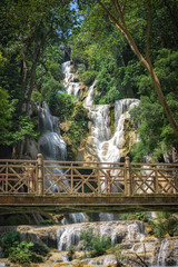 Beautiful large waterfall and old steel bridge structure in a deep green forest. Waterfall flowing over rocks. Nature background.