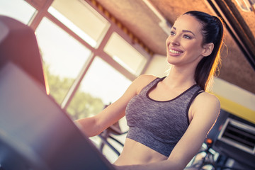 Smiling fit woman in sportswear walking on treadmill at gym
