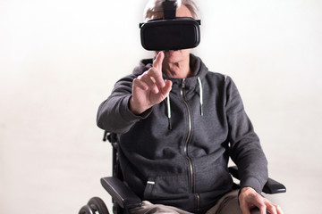 Aged man in wheelchair pointing his finger directly into camera while wearing VR glasses on his...