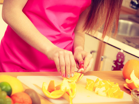 Woman housewife in kitchen cutting orange fruits
