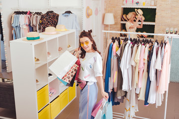 Shoes stand. Stylish happy shopaholic wearing bright clothes standing near shoes stand in showroom