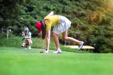 young woman golf player taking a golf ball in the hole on the green, with golfmate or challenger competitor exciting or enforcement in background, exciting or enforcement between players