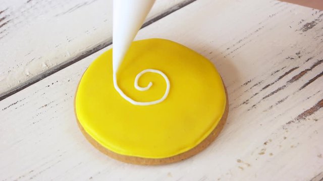 Piping a pattern on round yellow cookie. Decorating biscuit using piping bag. Guide for decoration of gingerbread cookies.