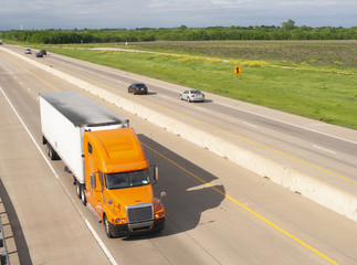 Fototapeta na wymiar Orange Semi Truck Trailer Rig Hauls Freight on Divided Highway