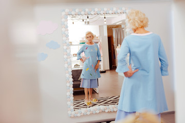 Blue costume. Blonde-haired retired woman trying blue costume on while standing near mirror in fitting room