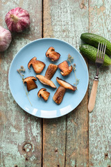 Nordic cuisine. Healthy vegan meal. Fried porcini (Boletus edulis) mushrooms row with raw cucumbers, garlic and thyme on shabby blue background