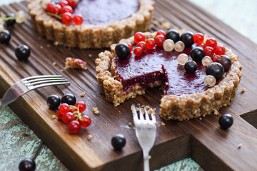 Small vegan tarts made of nuts and berry jam decorated with black, red and white currants on oak cutting board