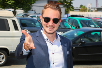 Autoverkäufer empfängt freundlich lächelnd seinen Kunden