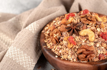 Wooden Bowl with granola with nuts, dried crandberries and dried orenge on a old light table