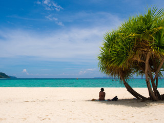 Fototapeta na wymiar Woman relaxing on white sand beach under palm tree with turquoise water sea and clear blue sky in sunny summer day for vacations holiday,copy space on left side.