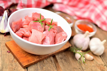 Raw pork meal diced in a bowl, garlic, half of onion, sweet pepper and checkered red tablecloth in the background