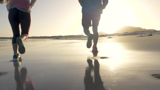 Low angle of couple jogging at sunset on a sandy beach