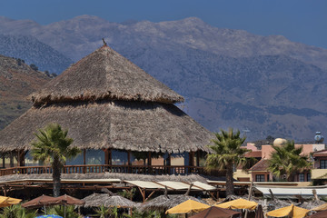Beach umbrellas, thatched roof of a beach cafe, mountains