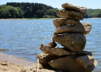 empilement de pierres en cairn sur le rivage d'un lac à l'eau miroitante