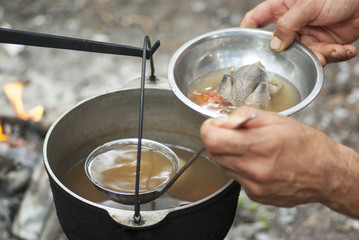 Pouring soup into a bowl with a ladle outdoor next to the fire.