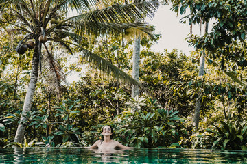 .Young and pretty woman enjoying her vacation in Ubud, in the Bali island, Indonesia. A summer afternoon in the pool with a tropical background. Relaxed and happy attitude. Lifestyle.