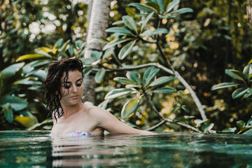 .Young and pretty woman enjoying her vacation in Ubud, in the Bali island, Indonesia. A summer afternoon in the pool with a tropical background. Relaxed and happy attitude. Lifestyle.