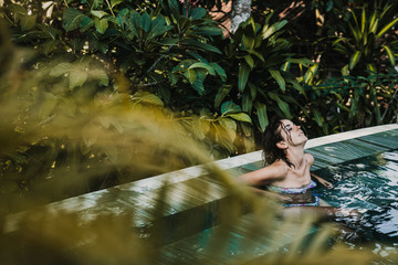 .Young and pretty woman enjoying her vacation in Ubud, in the Bali island, Indonesia. A summer afternoon in the pool with a tropical background. Relaxed and happy attitude. Lifestyle.