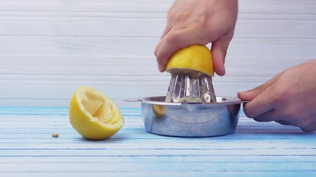 Hands Squeezing Fresh Organic Bio Lemons With Shiny Stainless Steel Juicer On Blue And White Blue Board Closeup