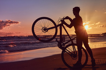 Fototapeta na wymiar Silhouette of a woman holds a bicycle on a sea coast on a sunset background.