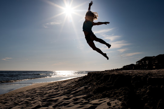 Girl jumping off sand dune with bright sun silhouette
