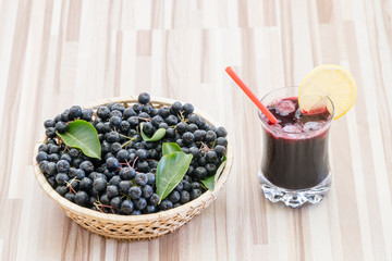 Fresh juice of chokeberry (Aronia melanocarpa) in glass and berry in pot on wooden background