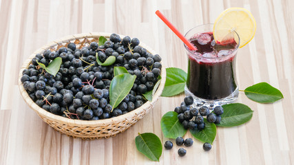 Fresh juice of chokeberry (Aronia melanocarpa) in glass and berry in pot on wooden background