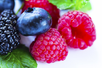 Close-up arrangement mixed, assorted berries including blackberries, strawberry, blueberry, raspberries and fresh leaf on white