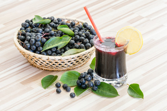 Fresh juice of chokeberry or Aronia melanocarpa in glass and berry in pot on wooden background