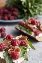 Sandwiches with whole grain bread, homemade cheese, arugula, ham and juicy raspberry. Healthy snack.