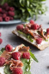 Sandwiches with whole grain bread, homemade cheese, arugula, ham and juicy raspberry. Healthy snack.