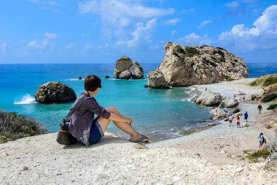 Dziewczyna siedząca na skale, w tle legendarne miejsce narodzin Afrodyty, Petra tou Romiou,  Cypru