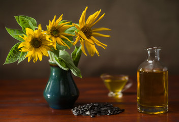 Still life with sunflowers in a vase, sunflower oil in a glass decanter and gravy boat, and a bunch of sunflower seeds. Selective focus.