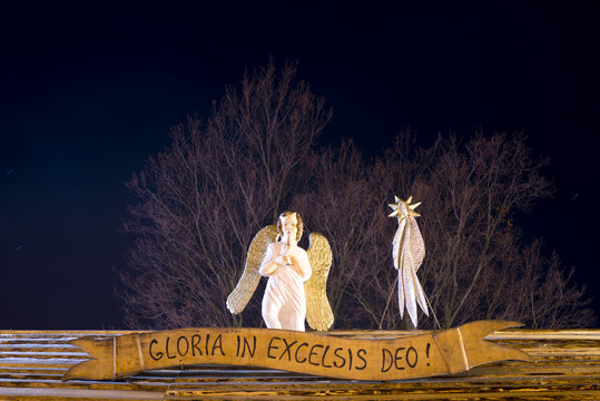 Night Christmas view on a wooden sculpture of an angle and comet star on wooden roof. Sign with reading Gloria in excelsis deo.