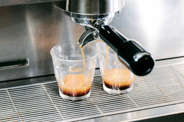 Close-up of espresso pouring from coffee machine. Professional coffee brewing by barista, two glasses.