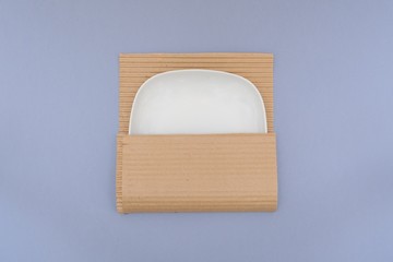 White plate in kraft paper on gray background. Concept of storage, feeling safe, protect,...